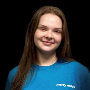 woman with long brown hair wearing a teal merry maids shirt standing in front of a black photo backdrop